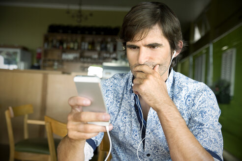 Mann in einem Café hört Musik vom Smartphone - TOYF000685