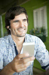 Lächelnder Mann hört Musik auf seinem Smartphone - TOYF000686