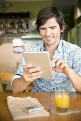 Lächelnder Mann in einem Café mit digitalem Tablet - TOYF000687