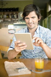 Smiling man in a cafe using digital tablet - TOYF000687