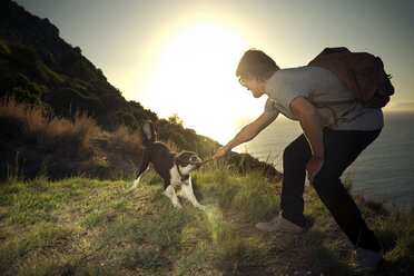 Südafrika, Mann spielt mit Hund an der Küste bei Sonnenuntergang - TOYF000806