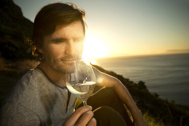 Südafrika, Mann Weißwein an der Küste bei Sonnenuntergang - TOYF000698