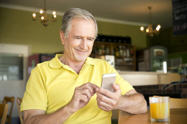 Porträt eines älteren Mannes mit Smartphone in einem Café - TOYF000732