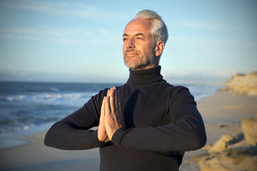 Südafrika, Porträt eines Mannes mit Rollkragenpullover, der vor Sonnenaufgang am Strand meditiert - TOYF000746