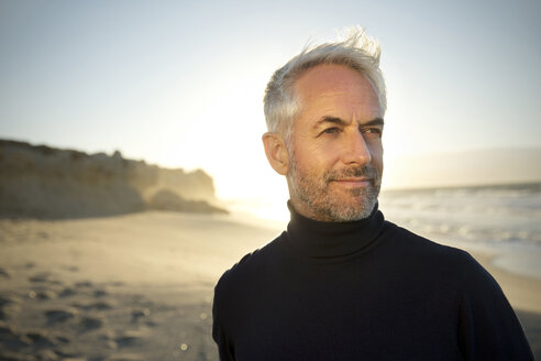 South Africa, portrait of white haired man wearing turtleneck standing on the beach before sunrise - TOYF000752