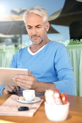 Porträt eines Mannes, der vor einem Café sitzt und ein digitales Tablet benutzt - TOYF000790