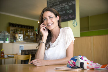 Porträt einer lächelnden Frau, die mit einem Smartphone in einem Café telefoniert - TOYF000793