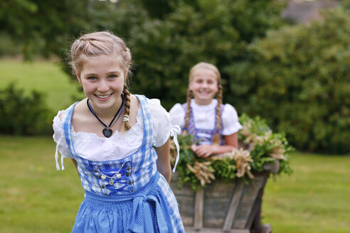 Deutschland, Lüneburger Heide, Porträt eines lächelnden blonden Mädchens im Dirndl beim Ziehen eines Erntewagens - HRF000029