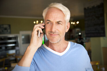 Porträt eines weißhaarigen Mannes, der mit einem Smartphone in einem Café telefoniert - TOYF000809