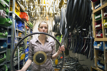 Junge Frau in einer Fahrradwerkstatt, die einen Reifen hält - SGF001603