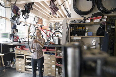 Young woman in a repair shop holding bicycle wheel - SGF001616