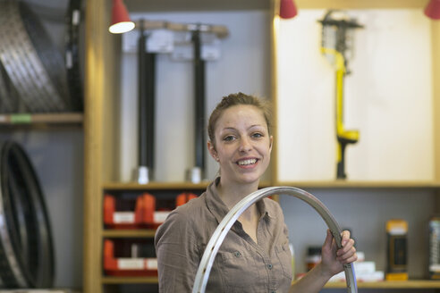 Lächelnde junge Frau in einer Reparaturwerkstatt, die ein Fahrradrad hält - SGF001611