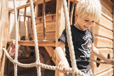 Lächelnder kleiner Junge, der auf einem Spielplatz über die Hängebrücke eines Holzschiffs läuft - MFF001623