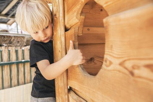 Kleiner Junge schaut in ein Loch eines Holzschiffs auf dem Spielplatz - MFF001626