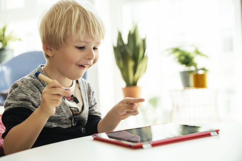 Glücklicher kleiner Junge mit digitalem Stift und digitalem Tablet zu Hause - MFF001631