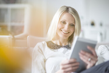 Portrait of smiling blond woman using mini tablet at home - CHPF000145