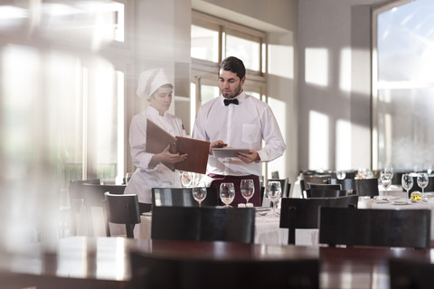 Koch und Kellner im Restaurant besprechen die Speisekarte, lizenzfreies Stockfoto