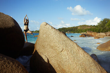 Seychelles, woman standing on a rock doing yoga exercise - ABF000604