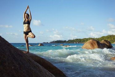 Seychelles, woman standing on a rock doing yoga exercise - ABF000605