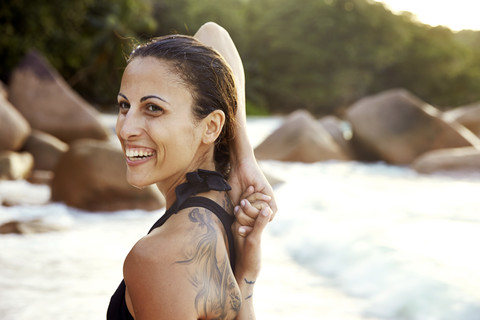 Seychellen, Porträt einer lächelnden Frau mit Tattoo bei einer Yoga-Übung am Strand, lizenzfreies Stockfoto