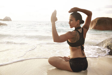 Seychelles, woman doing yoga exercise at seafront - ABF000625