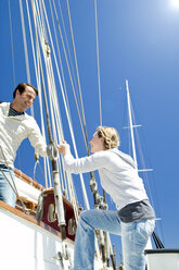 Reifer Mann hilft Frau beim Einsteigen auf ein Segelschiff - TOYF000814