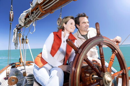 Glückliches reifes Paar am Ruder eines Segelschiffs - TOYF000819