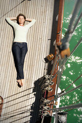 Relaxed mature woman lying on deck of a sailing ship - TOYF001038