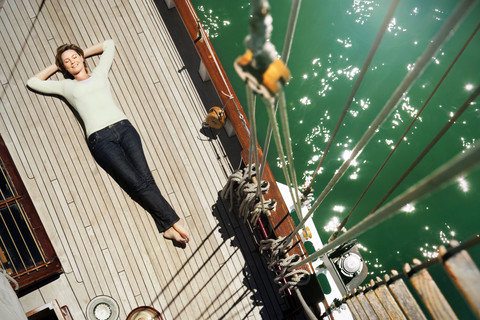 Entspannte reife Frau an Deck eines Segelschiffs liegend, lizenzfreies Stockfoto