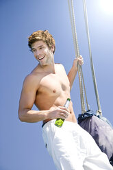 Young man on a sailing ship holding bottle of beer - TOYF000868