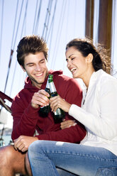 Happy young man and woman clinking beer bottles on a sailing ship - TOYF000885