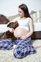 Pregnant woman sitting on the floor of her living room with her Labrador Retriever - SEGF000367