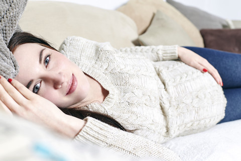 Porträt einer schwangeren Frau, die sich auf der Couch entspannt, lizenzfreies Stockfoto