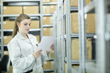 Young woman in storehouse looking at paper - SGF001623