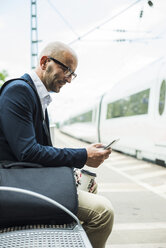 Businessman looking at cell phone on railway platform - UUF004406