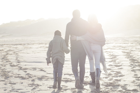 Südafrika, Kapstadt, Rückenansicht einer Familie, die bei Gegenlicht am Strand spazieren geht, lizenzfreies Stockfoto