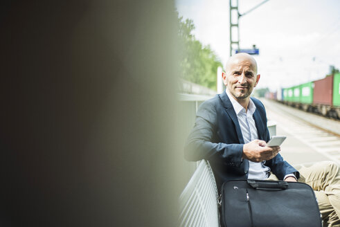 Geschäftsmann mit Mobiltelefon auf dem Bahnsteig - UUF004409