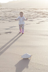 Baby girl standing on the beach looking at a shell - ZEF005256
