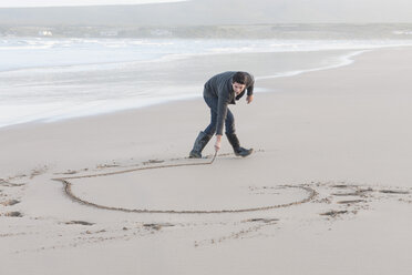 South Africa, Cape Town, man scratching heart in the sandy beach - ZEF005276