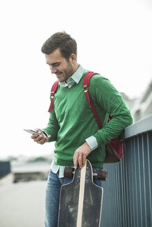 Mann mit Longboard schaut auf sein Handy - UUF004426