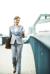 Businesswoman walking on bridge looking at cell phone - UUF004428