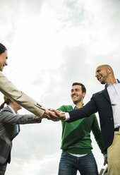 Four happy businesspeople stacking their hands outdoors - UUF004436