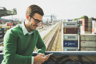 Man at freight yard looking at cell phone - UUF004442