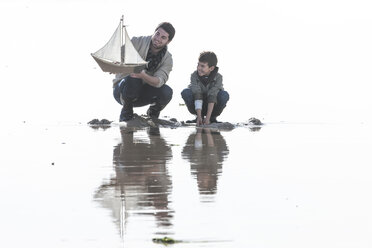 Vater und Sohn mit Spielzeug-Segelboot am Strand - ZEF005426