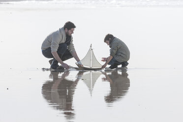 Vater und Sohn spielen mit einem Spielzeug-Segelboot an der Strandpromenade - ZEF005307