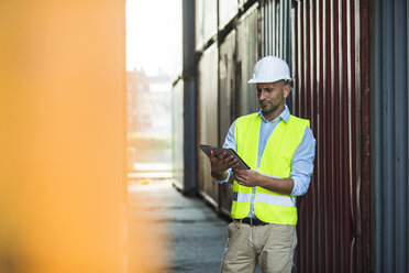 Man with digital tablet wearing reflective vest at container port - UUF004457