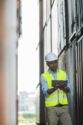 Man with digital tablet wearing reflective vest at container port - UUF004459