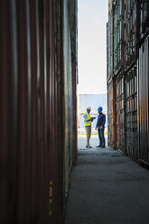 Two men with safety helmets talking at container port - UUF004460