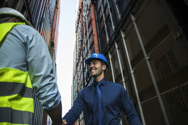 Two men with safety helmets at container port shaking hands - UUF004465