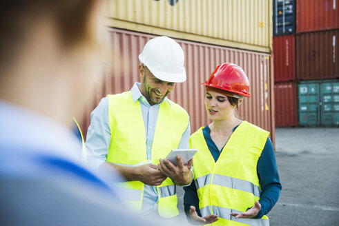 Frau und lächelnder Mann mit Sicherheitshelmen und digitalem Tablet im Containerhafen - UUF004467